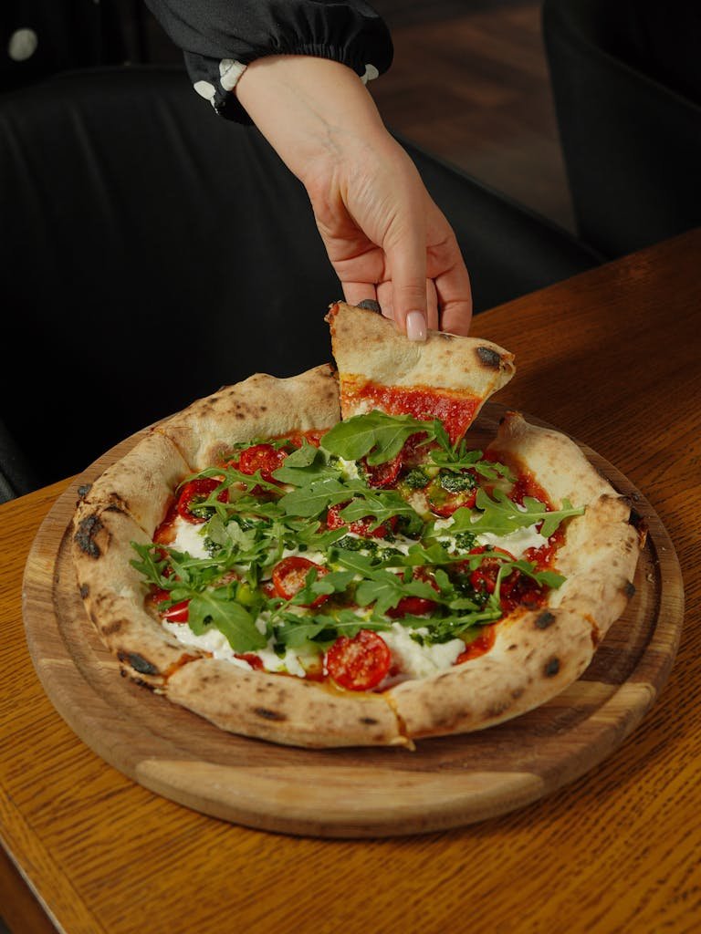 Tasty arugula pizza with a hand grabbing a slice, perfect for foodies and restaurant promotions.